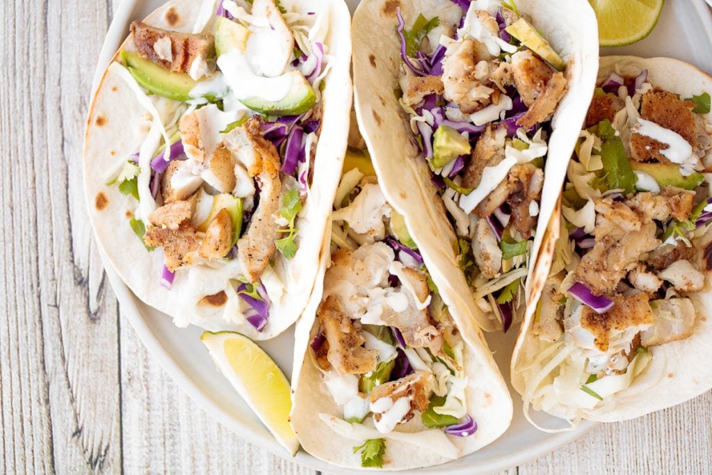 Flavourful, easy fish tacos with lime crema is made with seasoned white fish, cabbage slaw, and lime sauce. It takes less than 25 minutes to prep and serve. | aheadofthyme.com