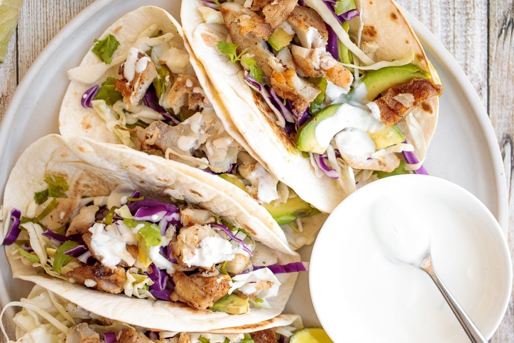 Flavourful, easy fish tacos with lime crema is made with seasoned white fish, cabbage slaw, and lime sauce. It takes less than 25 minutes to prep and serve. | aheadofthyme.com