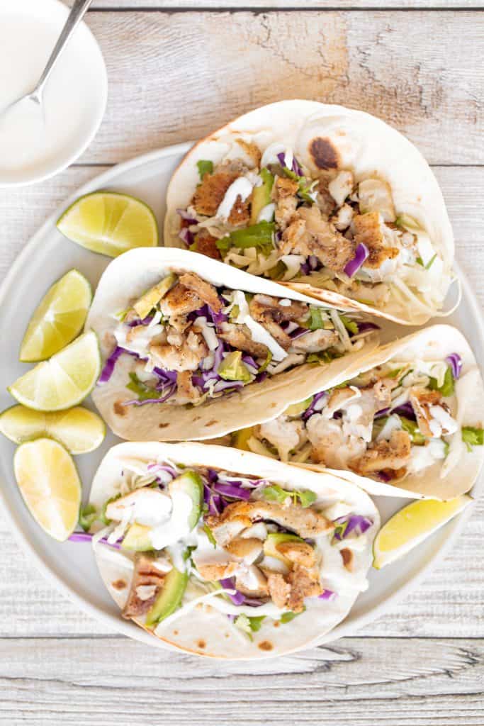Flavourful, easy fish tacos with lime crema is made with seasoned white fish, cabbage slaw, and lime sauce. It takes less than 25 minutes to prep and serve. | aheadofthyme.com