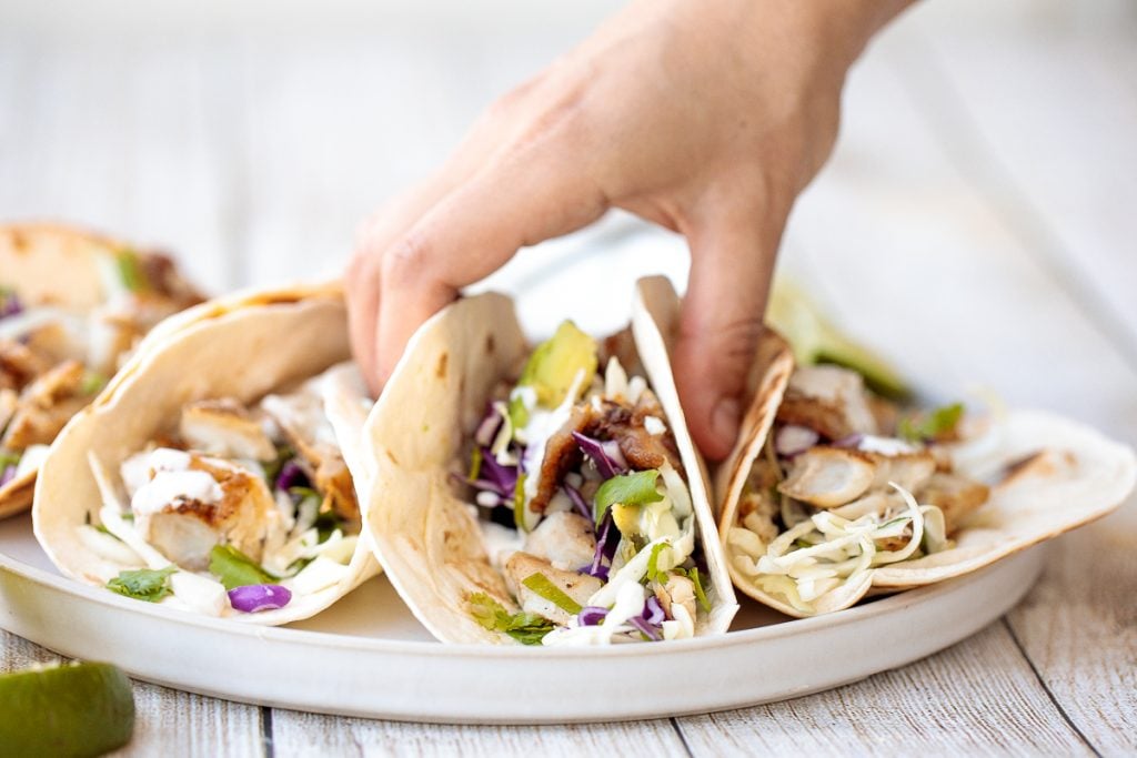 Flavourful, easy fish tacos with lime crema is made with seasoned white fish, cabbage slaw, and lime sauce. It takes less than 25 minutes to prep and serve. | aheadofthyme.com