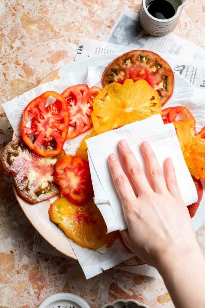 Patting sliced tomatoes dry with paper towels.