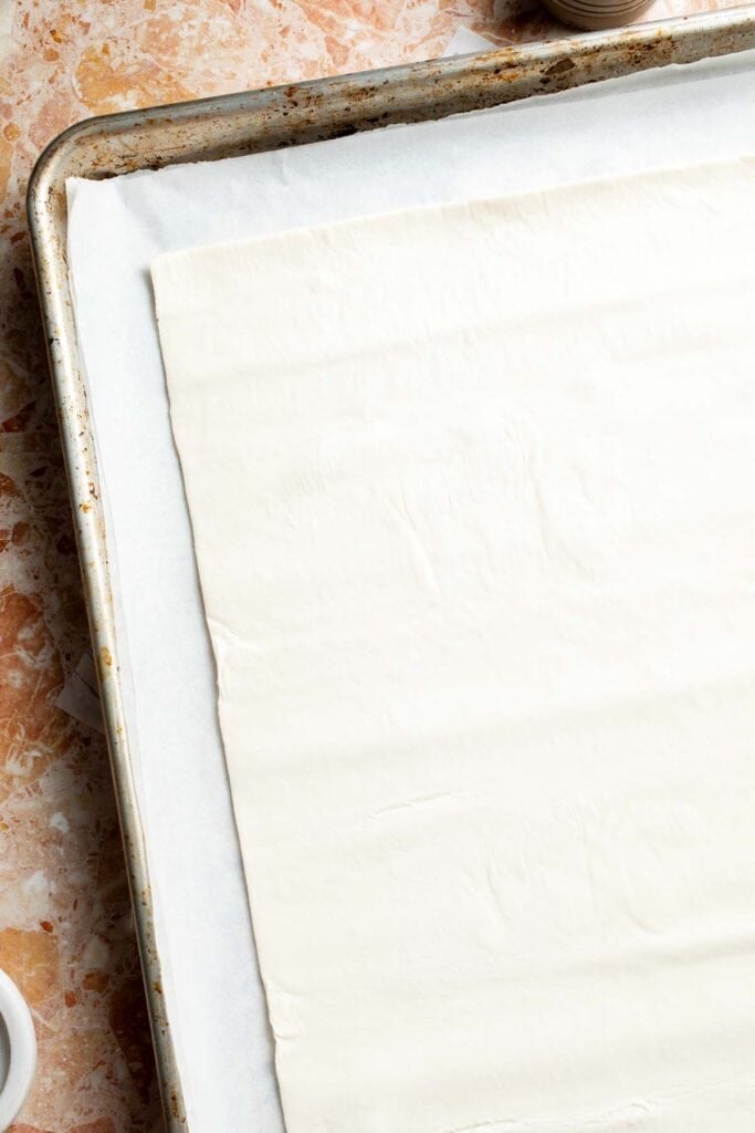 Puff pastry sheet arranged on a parchment-lined baking sheet.