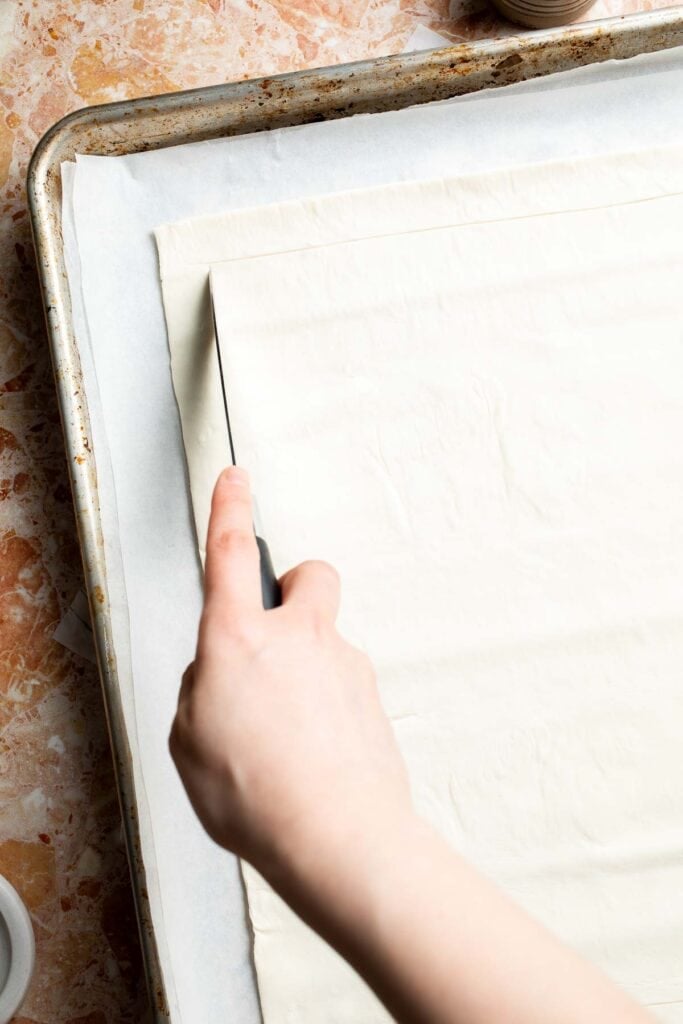 Scoring a border around the puff pastry with a sharp knife.