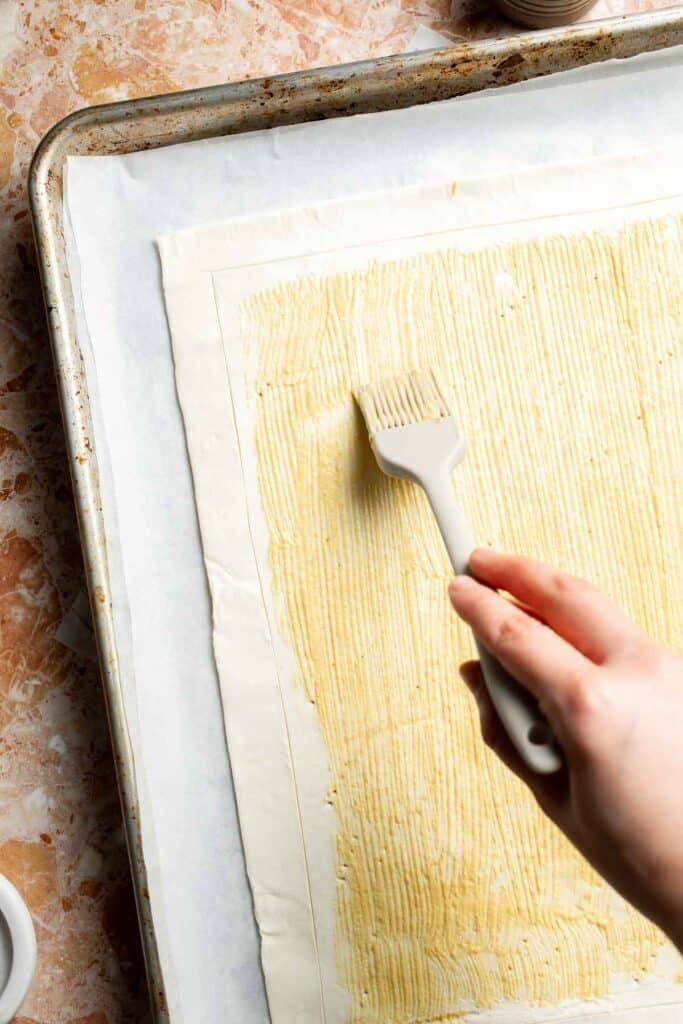 Brushing the puff pastry with Dijon mustard.