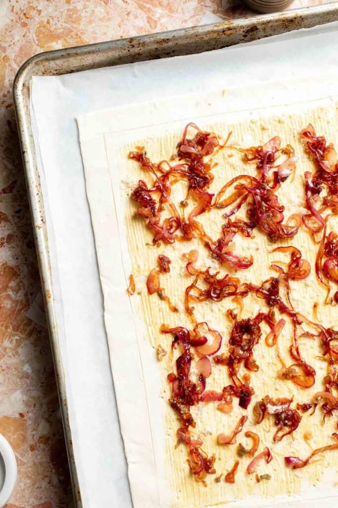Adding caramelized onions over the puff pastry.