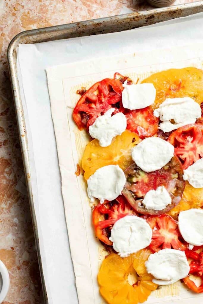 Adding fresh mozzarella slices between the tomatoes.