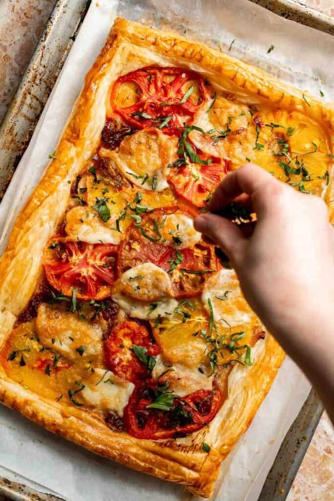 Adding fresh basil to the baked Tomato Puff Pastry Tart.