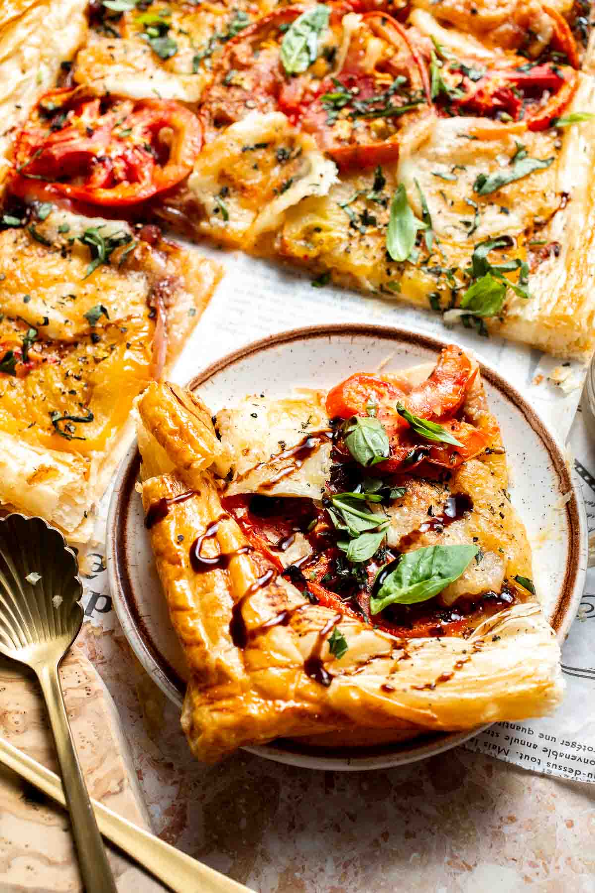 Slice of Tomato Puff Pastry Tart with mozzarella, tomatoes, caramelized onions, and basil.