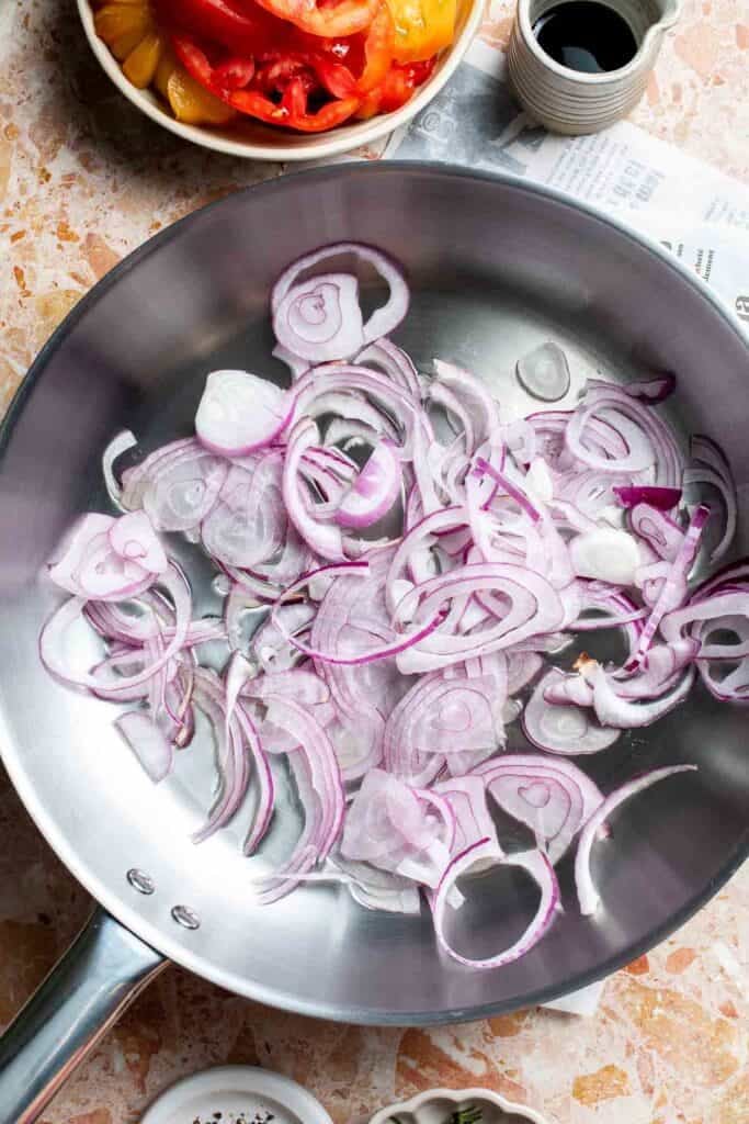 Sautéing sliced red onions in a skillet.