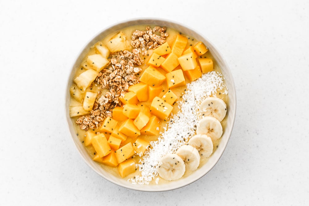 Mango pineapple tropical smoothie bowl? Yes, please! Who doesn't love pineapples and mangos blended together and topped with more fruit, granola, and coconut? | aheadofthyme.com