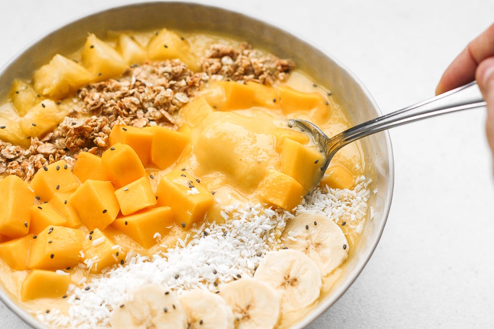 Mango pineapple tropical smoothie bowl? Yes, please! Who doesn't love pineapples and mangos blended together and topped with more fruit, granola, and coconut? | aheadofthyme.com