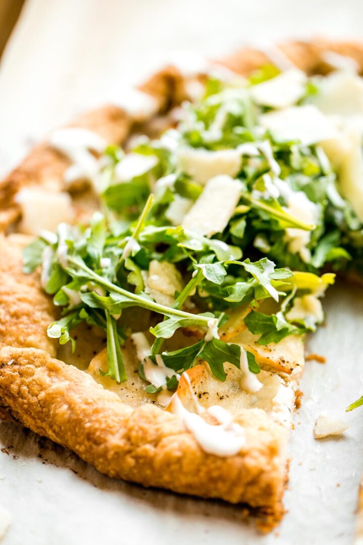 A perfectly baked golden potato galette topped with a fresh arugula salad and swirls of creamy crème fraîche.