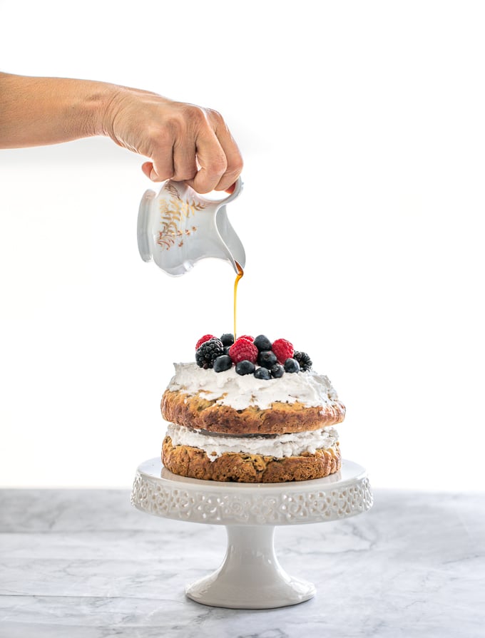 This healthy banana smash cake is held together with a whipped coconut cream frosting and topped with more cream, mixed berries and a drizzle of maple syrup. | aheadofthyme.com