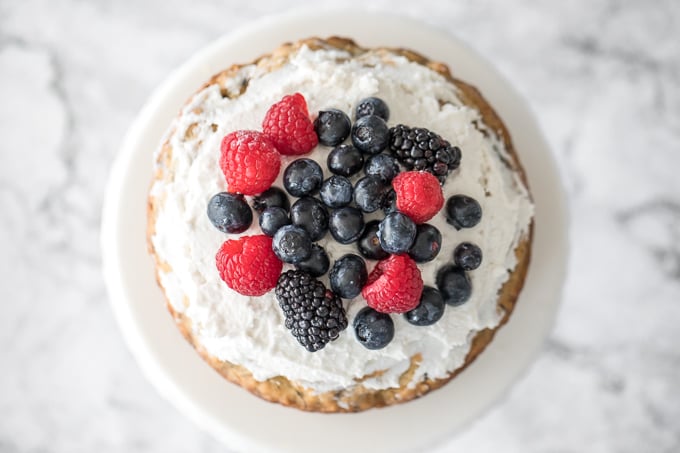 This healthy banana smash cake is held together with a whipped coconut cream frosting and topped with more cream, mixed berries and a drizzle of maple syrup. | aheadofthyme.com