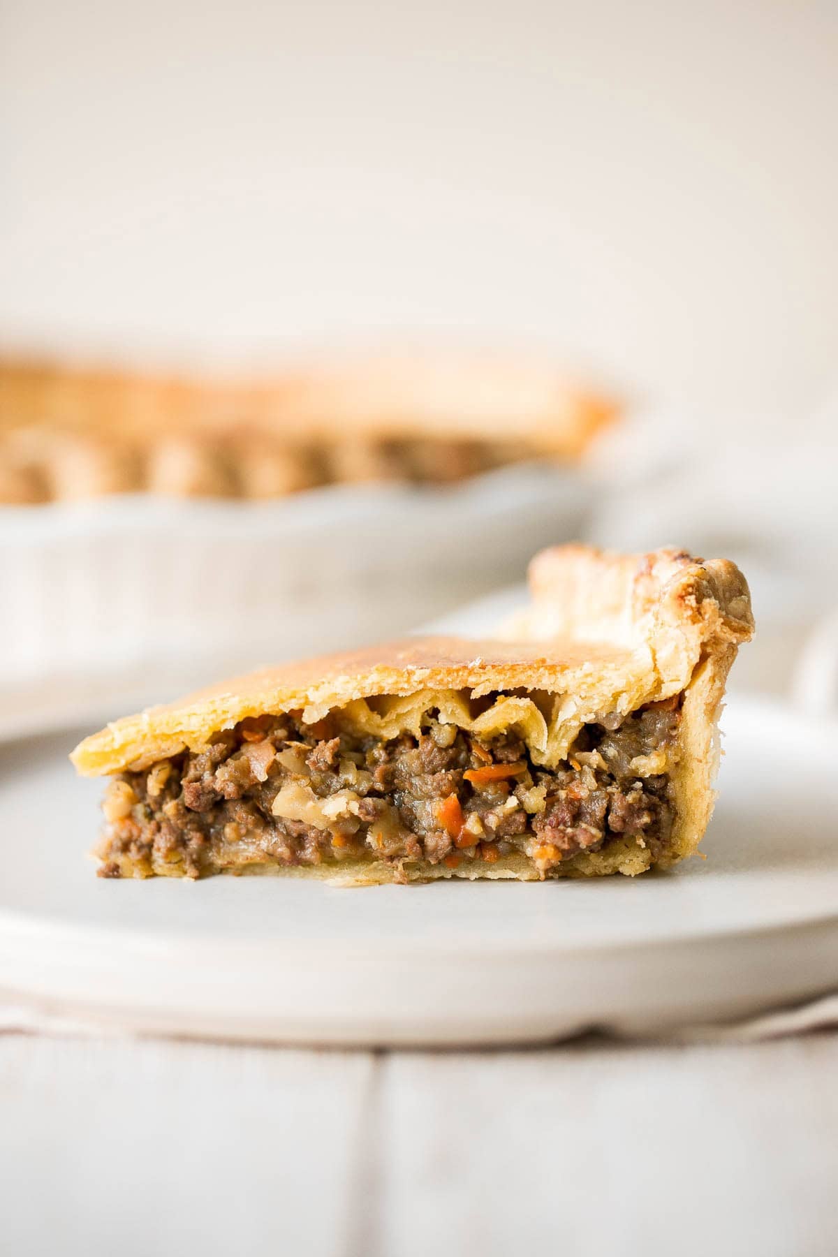 Close-up slice of ground beef meat pie on a plate, showing the seasoned filling and flaky crust layers