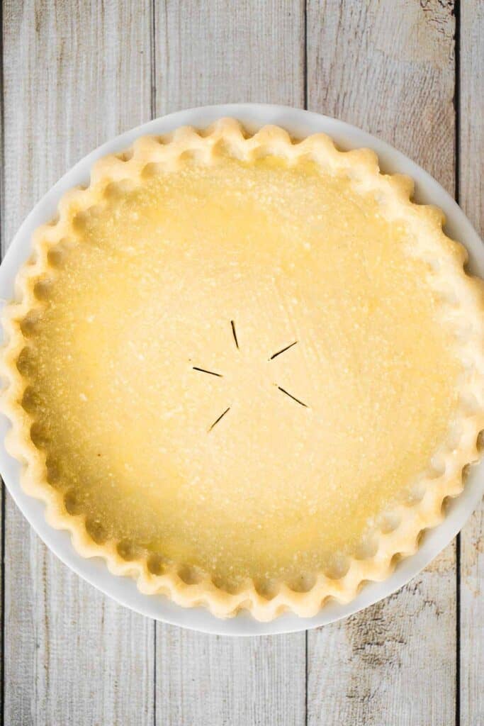 Unbaked meat pie with a fluted crust and five vent slits cut into the top and egg wash added