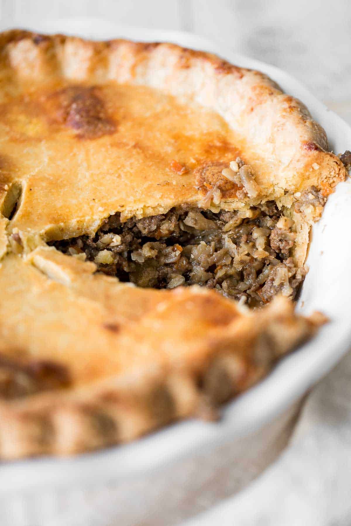 Close-up of a baked ground beef meat pie with a slice cut out, showing the seasoned filling inside a golden, flaky crust