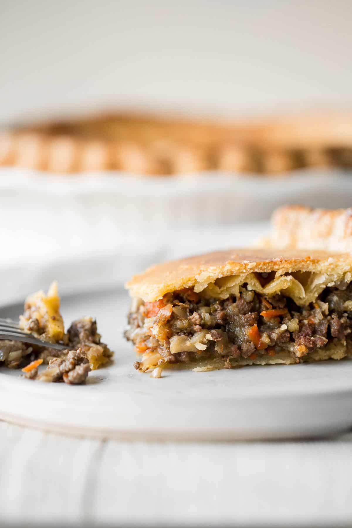 Close-up of a slice of ground beef meat pie on a plate, showing the layered filling and flaky crust