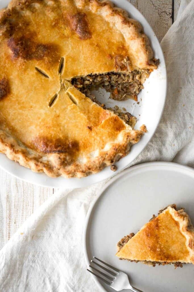 Overhead view of a baked ground beef meat pie with a slice removed and served on a separate plate