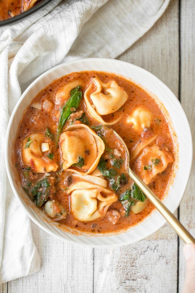 Hearty and creamy tortellini soup with sausage, spinach and kale is total comfort food in a bowl. Make this flavourful one pot meal in under 30 minutes. | aheadofthyme.com