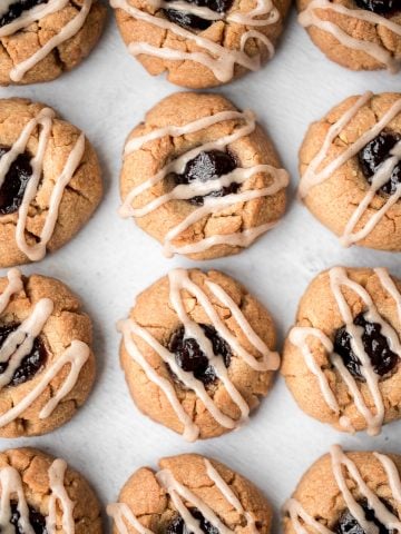 Melt-in-your-mouth peanut butter thumbprint cookies with raspberry jam and a drizzle of maple cinnamon glaze are the best holiday cookies and easy to make. | aheadofthyme.com