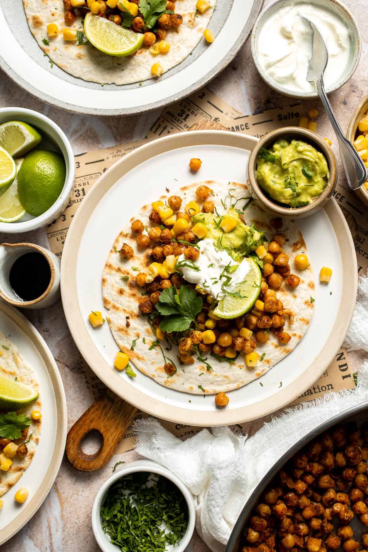 Overhead view of healthy vegan chickpea tacos with guacamole, corn, cilantro, and lime wedges.