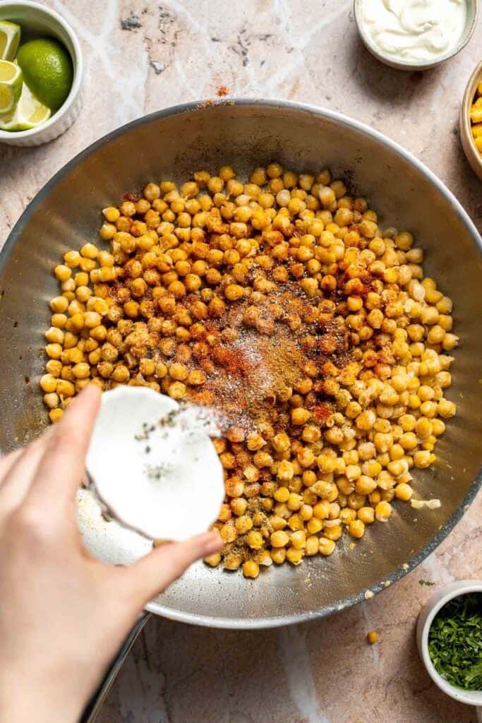 Salt and pepper sprinkled over chickpeas in a skillet.