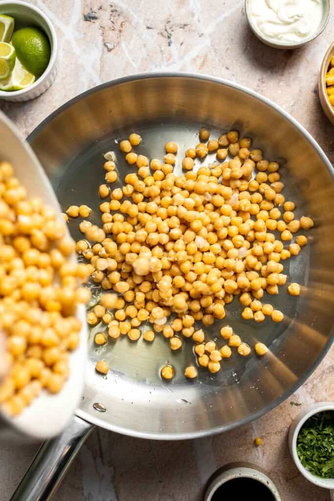Chickpeas being added to a skillet with hot oil.