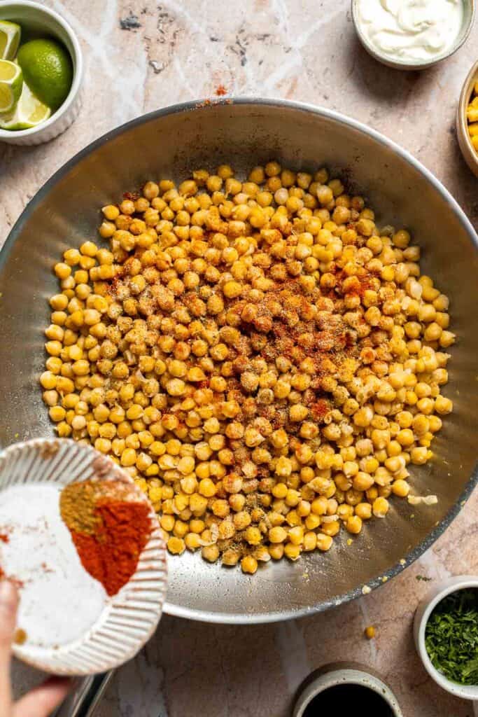 Taco seasonings being added to sautéed chickpeas.