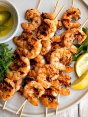 Grilled garlic shrimp skewers served with fresh parsley, lemon slices, and olive oil.