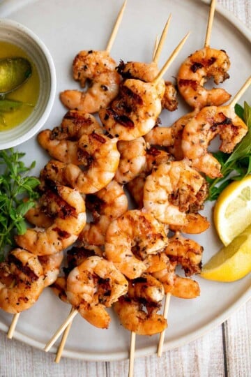 Grilled garlic shrimp skewers served with fresh parsley, lemon slices, and olive oil.