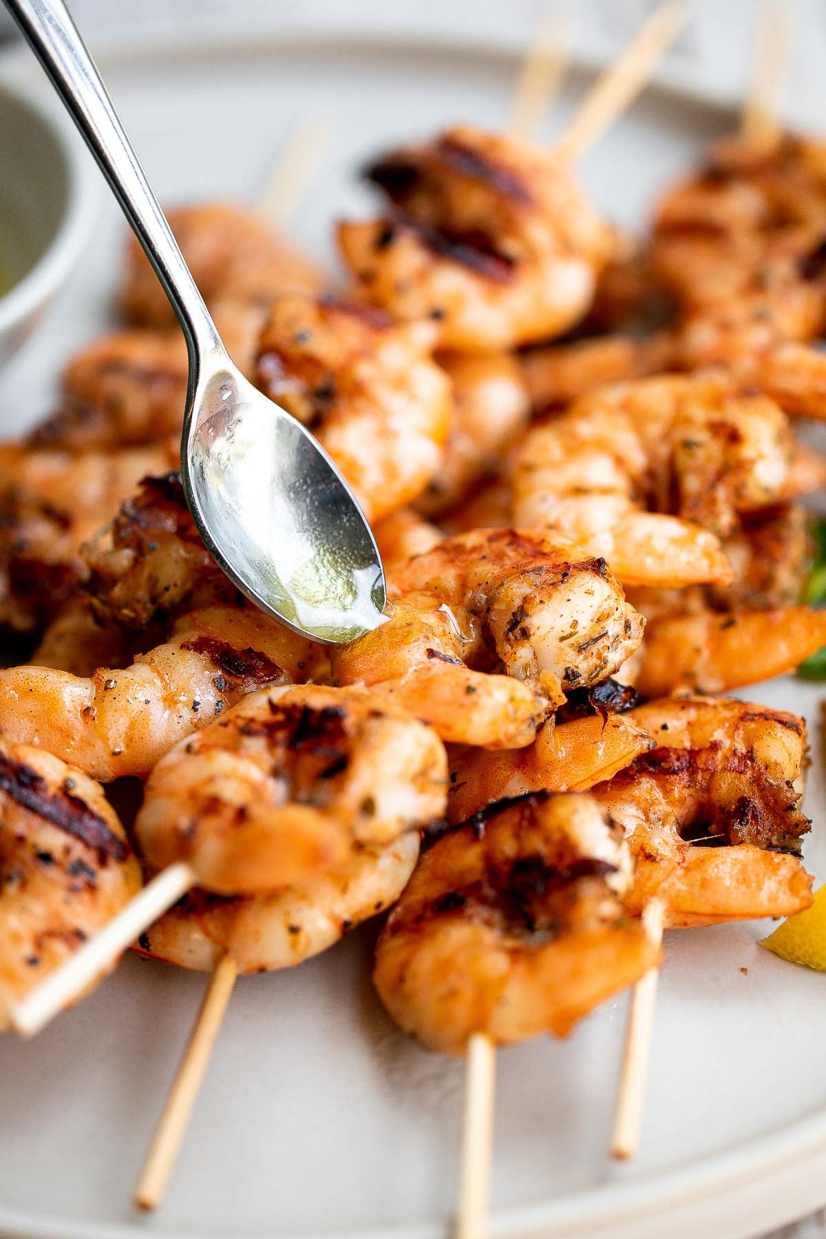 Spoon drizzling sauce over grilled garlic shrimp skewers.
