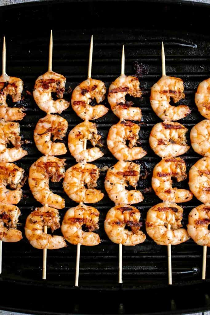Garlic shrimp skewers cooking on a hot outdoor grill.