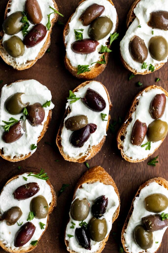 Whipped feta crostini with a herby olive topping is quick and easy snack or appetizer that is ready in less than 20 minutes — or 10 minutes if you’re fast. | aheadofthyme.com