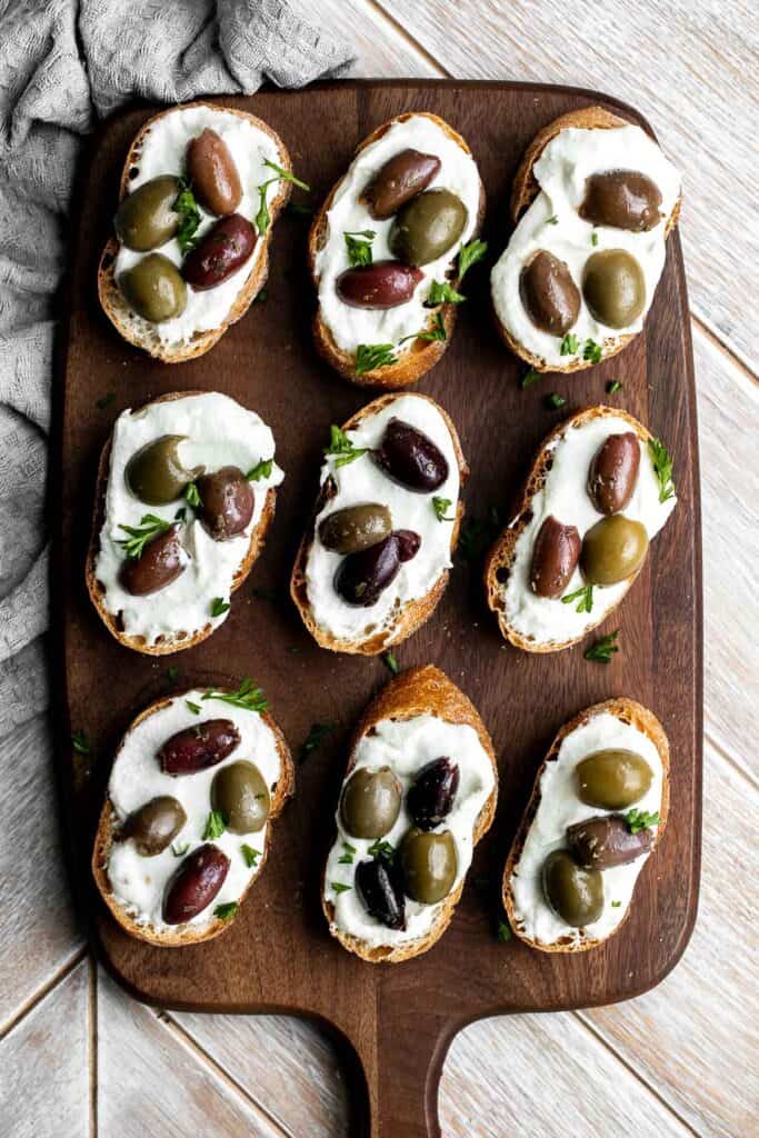 Whipped feta crostini with a herby olive topping is quick and easy snack or appetizer that is ready in less than 20 minutes — or 10 minutes if you’re fast. | aheadofthyme.com