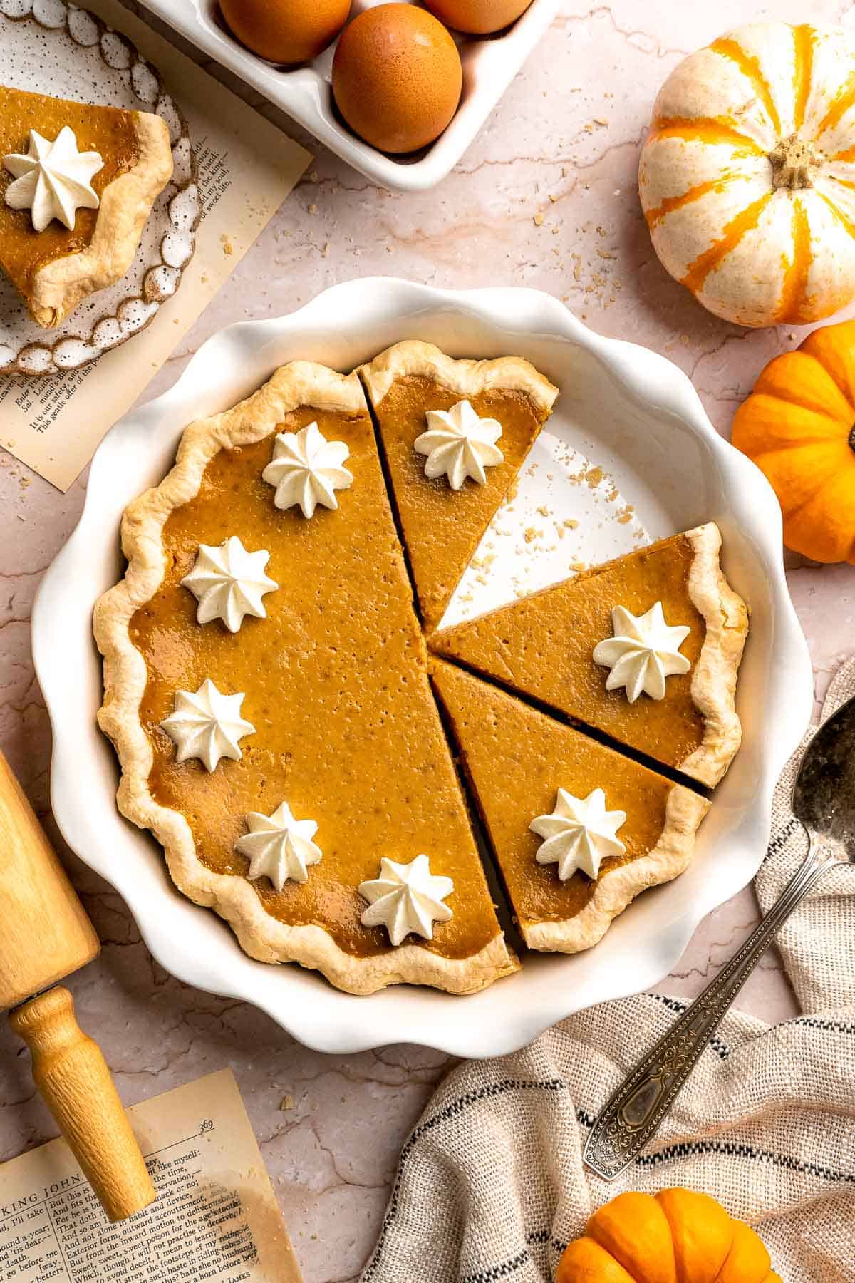 Homemade pumpkin pie in a white fluted pie dish, topped with whipped cream rosettes, with slices cut and one slice removed.