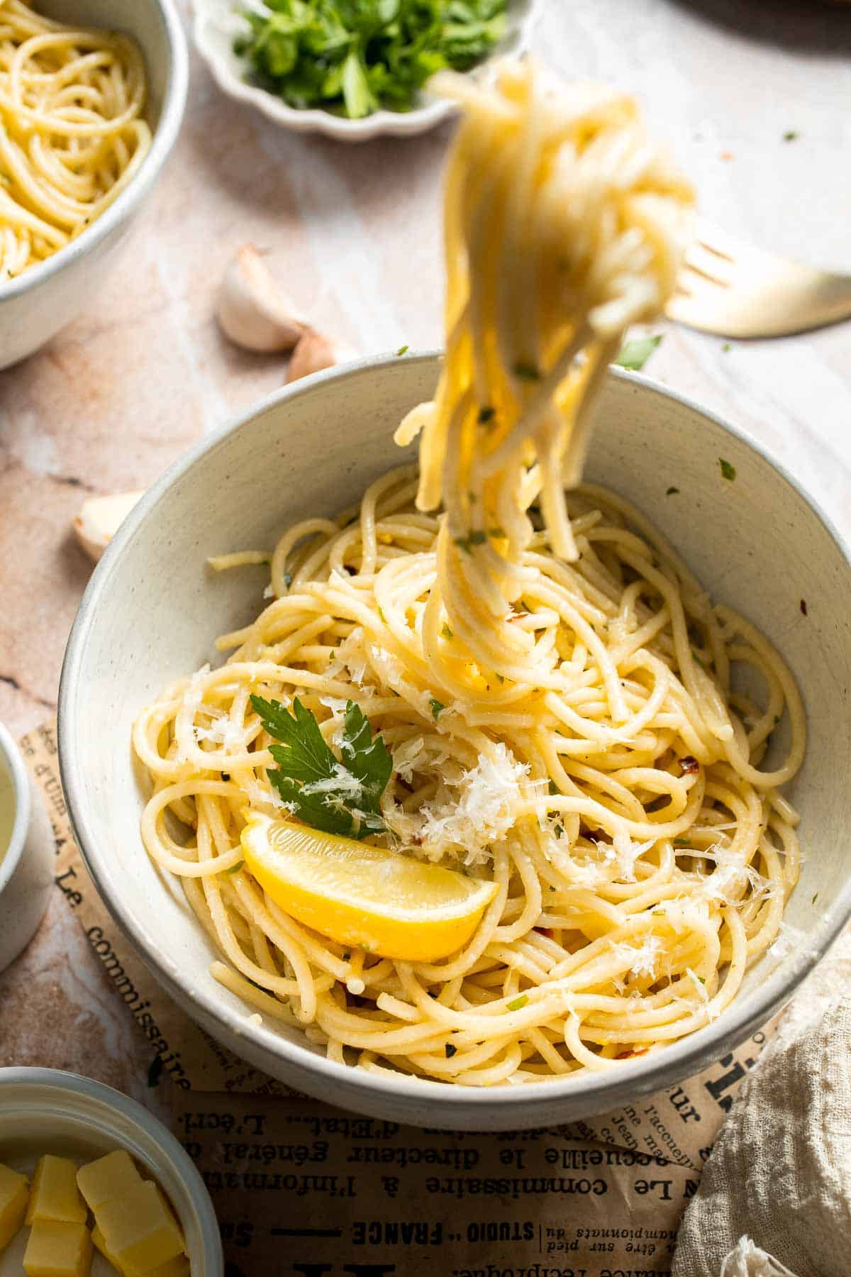 Fork twirling lemon butter pasta with Parmesan cheese, parsley, and fresh lemon.