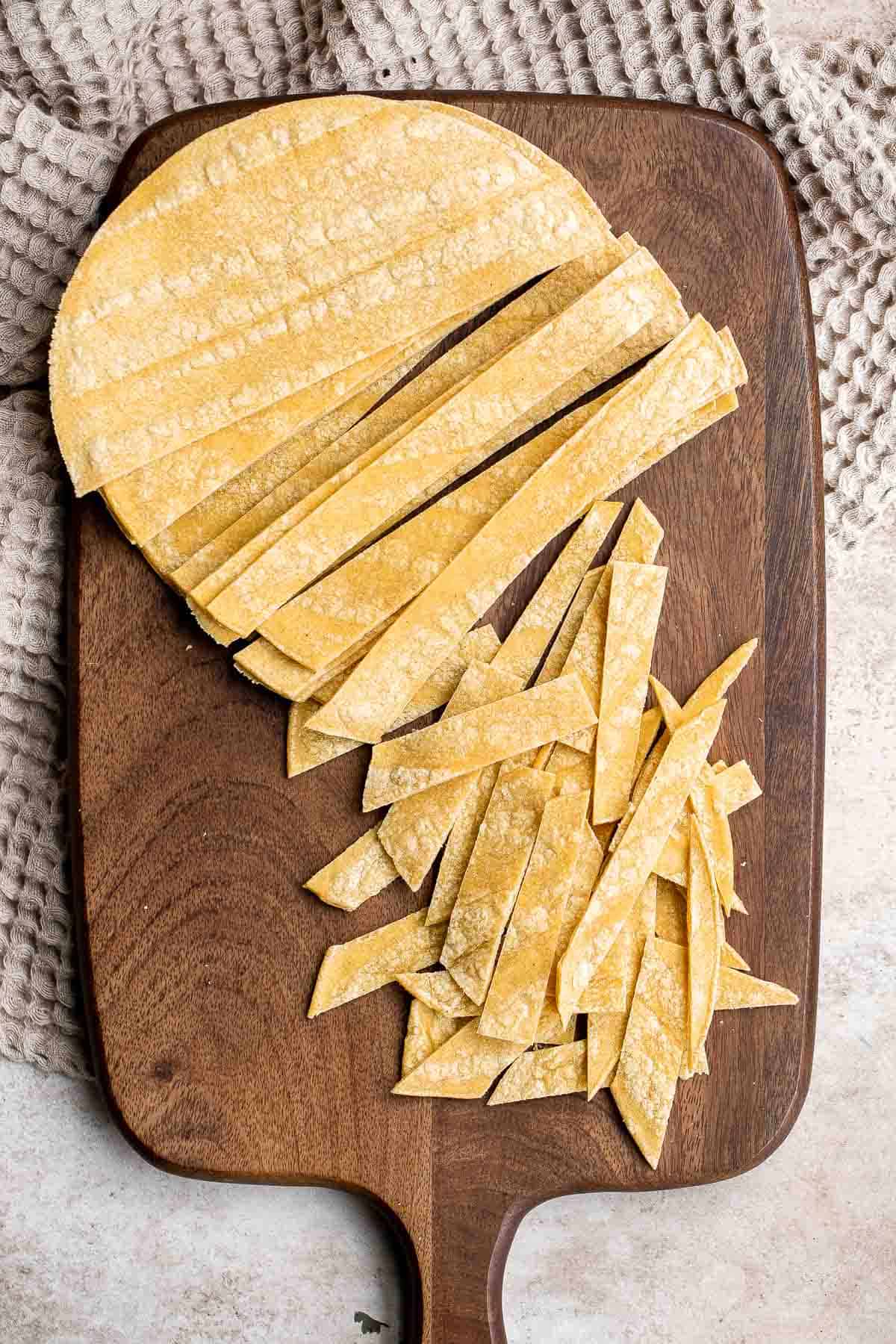 Tortillas on a cutting board with half of them cut into 1/2-inch strips. | aheadofthyme.com
