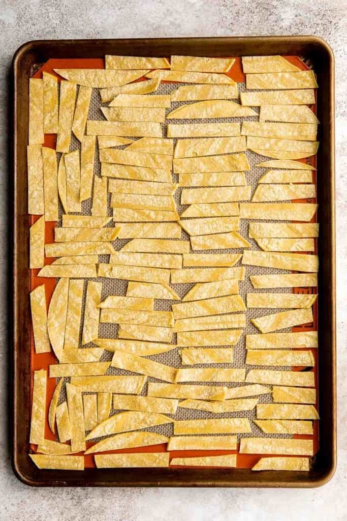 Uncooked tortilla strips spaced evenly apart on a large baking sheet. | aheadofthyme.com