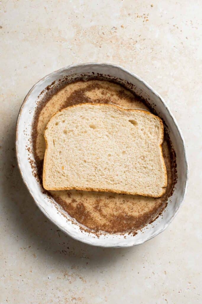 Slice of bread dipping into egg mixture for French toast. | aheadofthyme.com