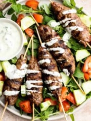 Beef Kofta Kebabs served over a fresh cucumber and tomato salad with creamy yogurt sauce drizzled on top.