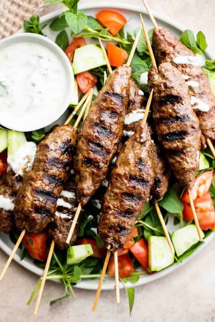 Beef Kofta Kebabs with creamy yogurt sauce served over a fresh Mediterranean salad.