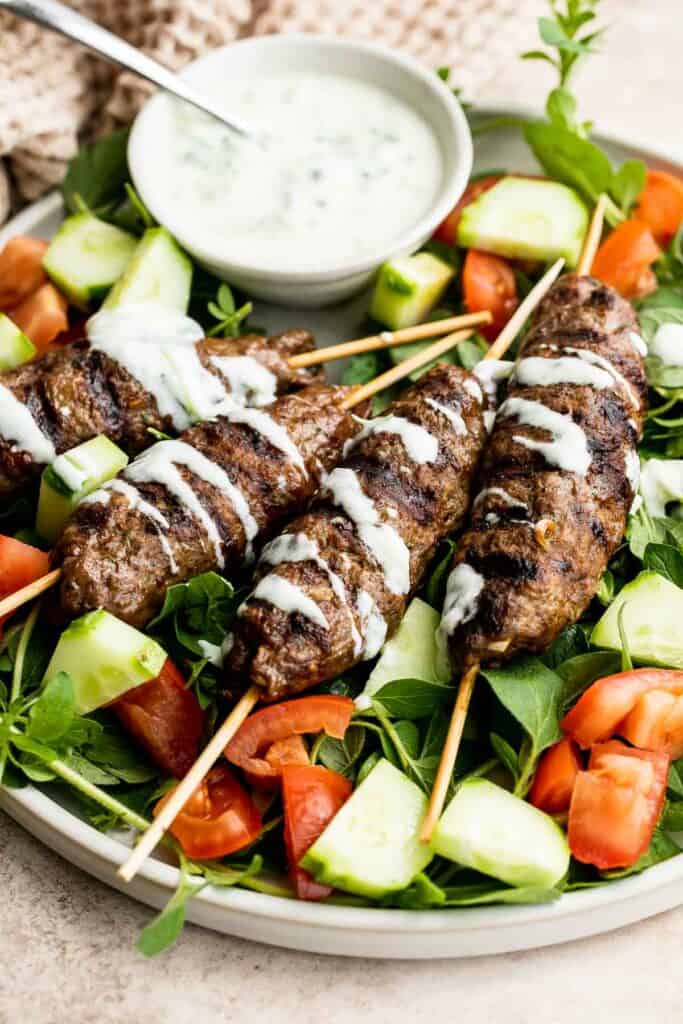 Beef Kofta Kebabs drizzled with yogurt sauce and served with a fresh cucumber and tomato salad.