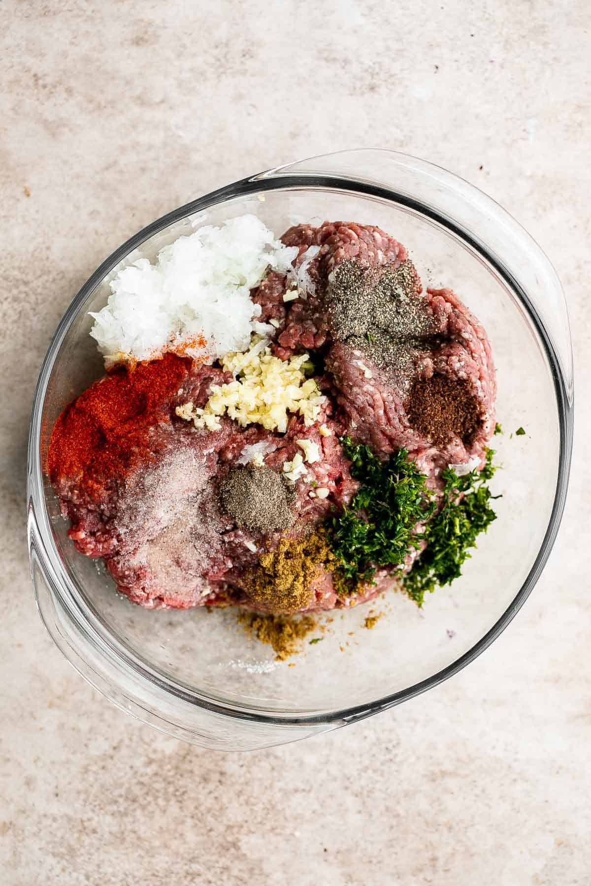 Ingredients for Beef Kofta Kebabs including ground beef, onion, garlic, parsley, and spices in a mixing bowl.