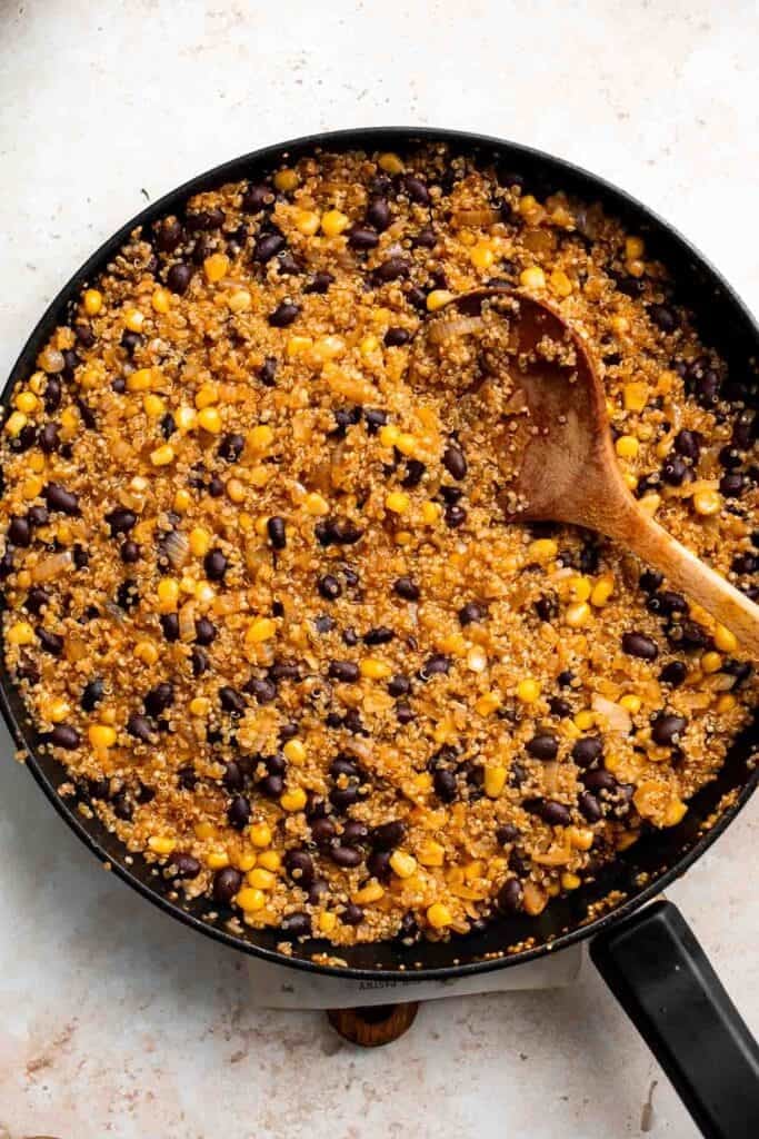 Quinoa, black bean, and corn filling cooking in a skillet, stirred with a wooden spoon