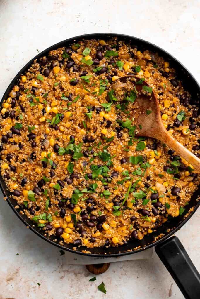 Quinoa, black bean, and corn filling cooking in a skillet, stirred with a wooden spoon
