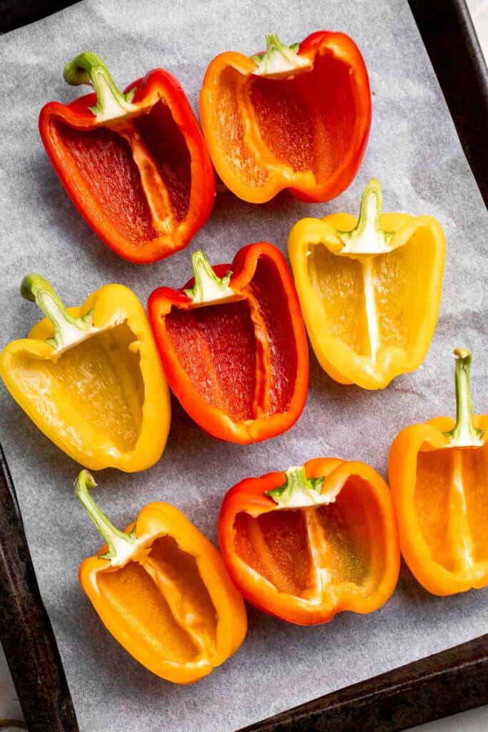 Halved red and yellow bell peppers before stuffing, arranged on a baking sheet