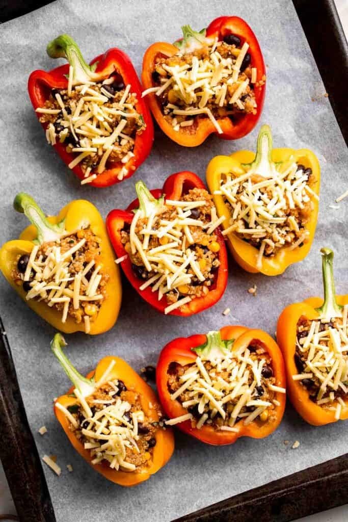 Overhead view of vegetarian quinoa stuffed peppers on parchment paper topped with shredded cheese