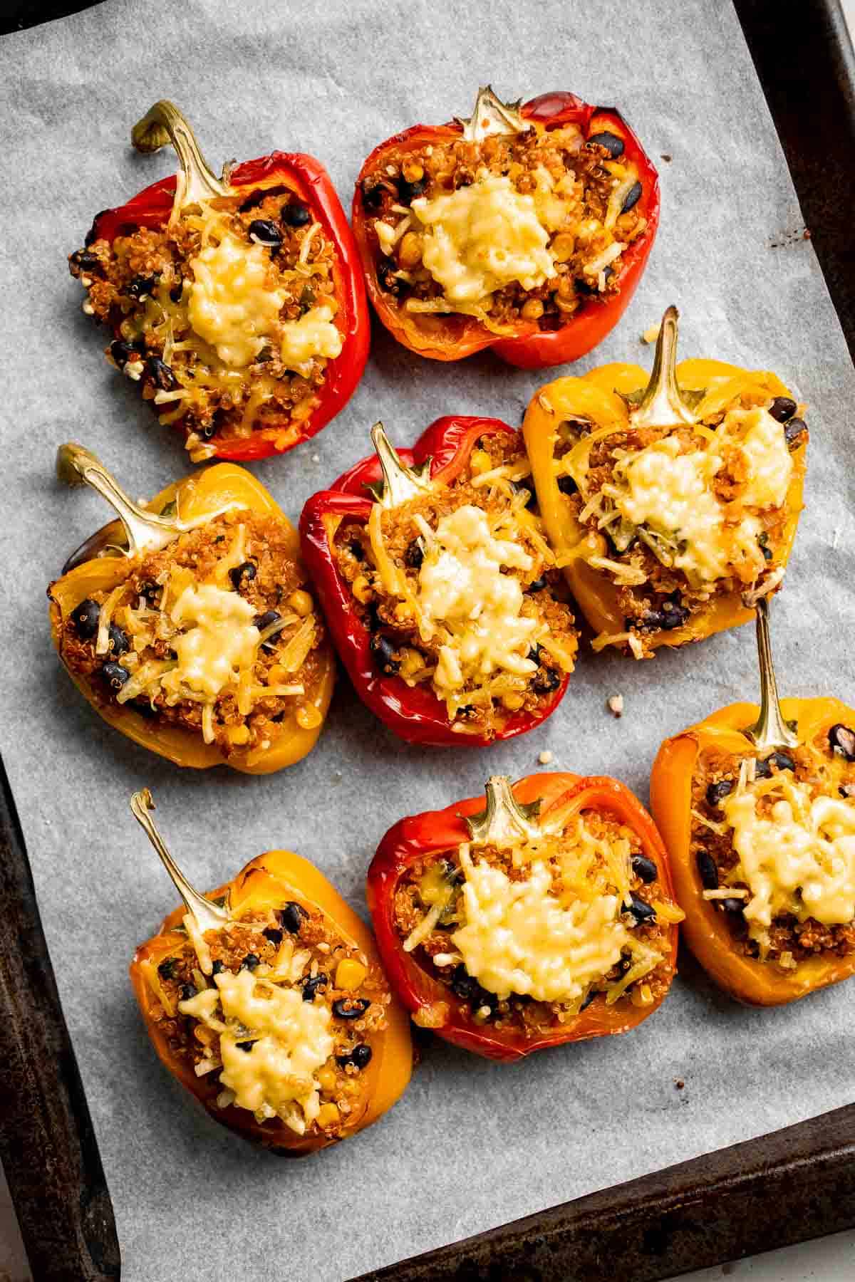 Overhead view of baked vegetarian quinoa stuffed peppers with melted cheese on a baking sheet