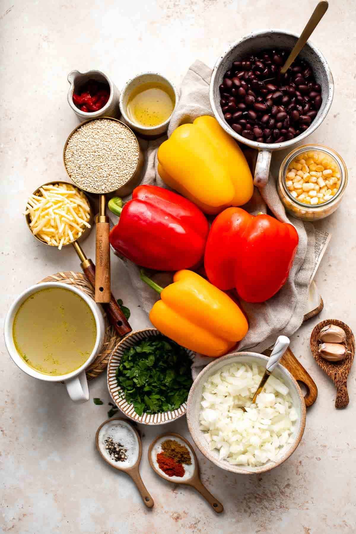 Ingredients for vegetarian quinoa stuffed peppers including bell peppers, quinoa, black beans, corn, garlic, cheese, and spices